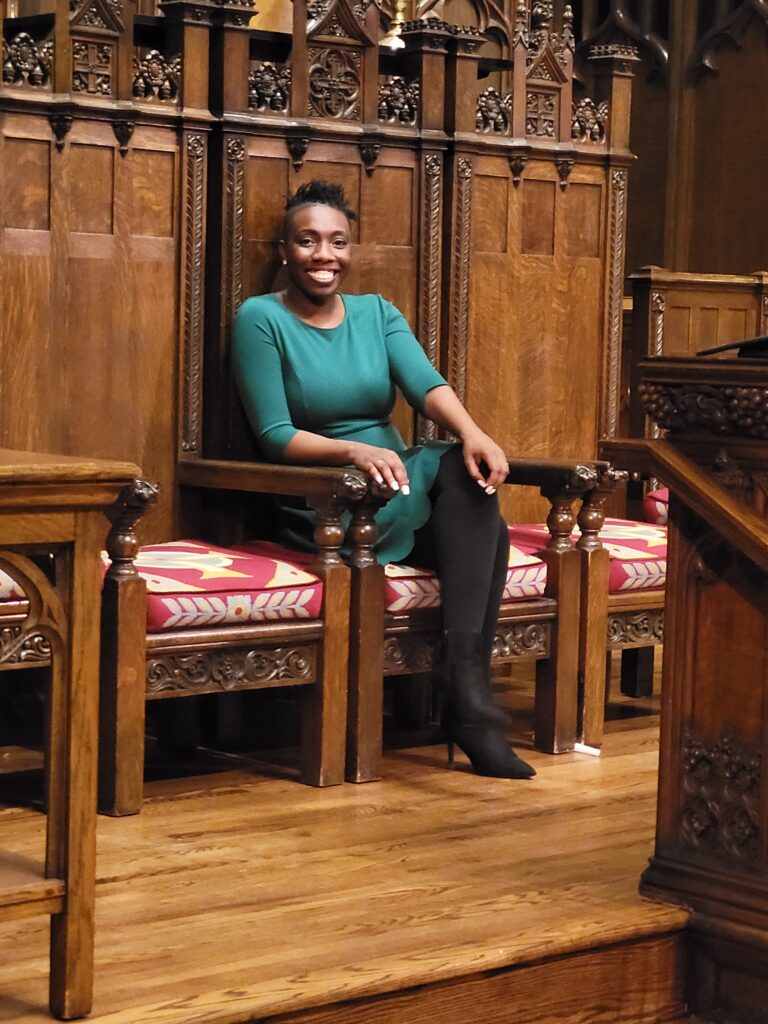 Me smiling wearing a green dress siting on high back wooden brown chair with ornate carvings