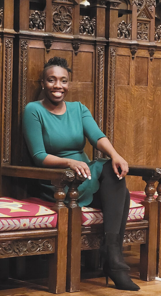 Me smiling wearing a green dress siting on high back wooden brown chair with ornate carvings