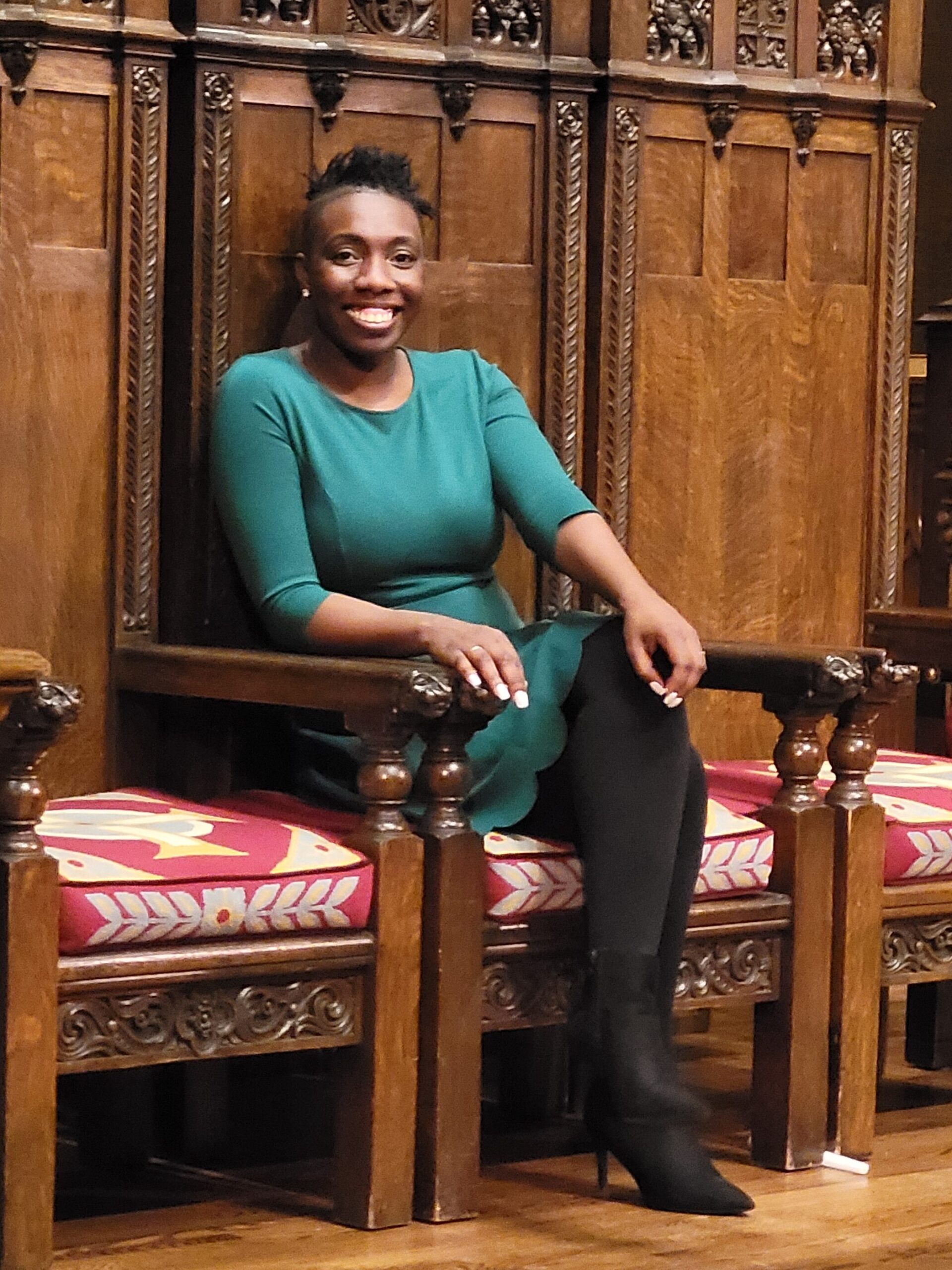 Me smiling wearing a green dress siting on high back wooden brown chair with ornate carvings
